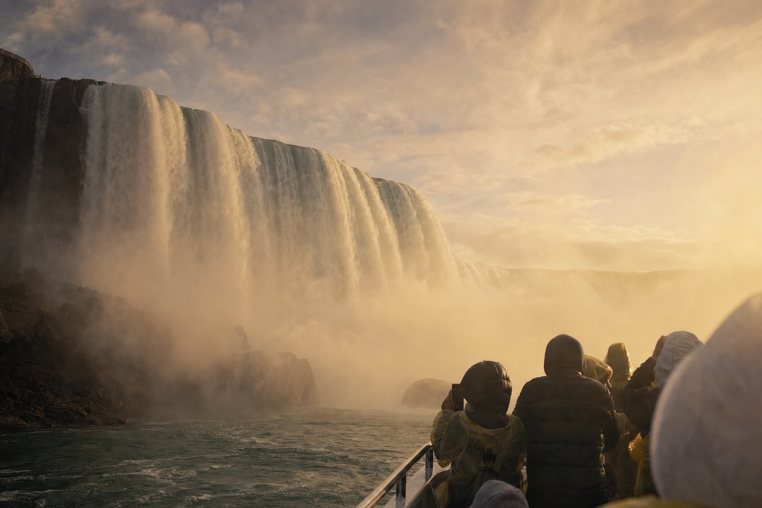 The falls in low golden September light seen from the water, thin crowds at the rails and warm tones in the spray