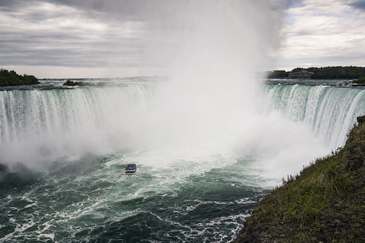 The falls in late spring with a visibly swollen flow and a huge spray column, an almost empty boat below