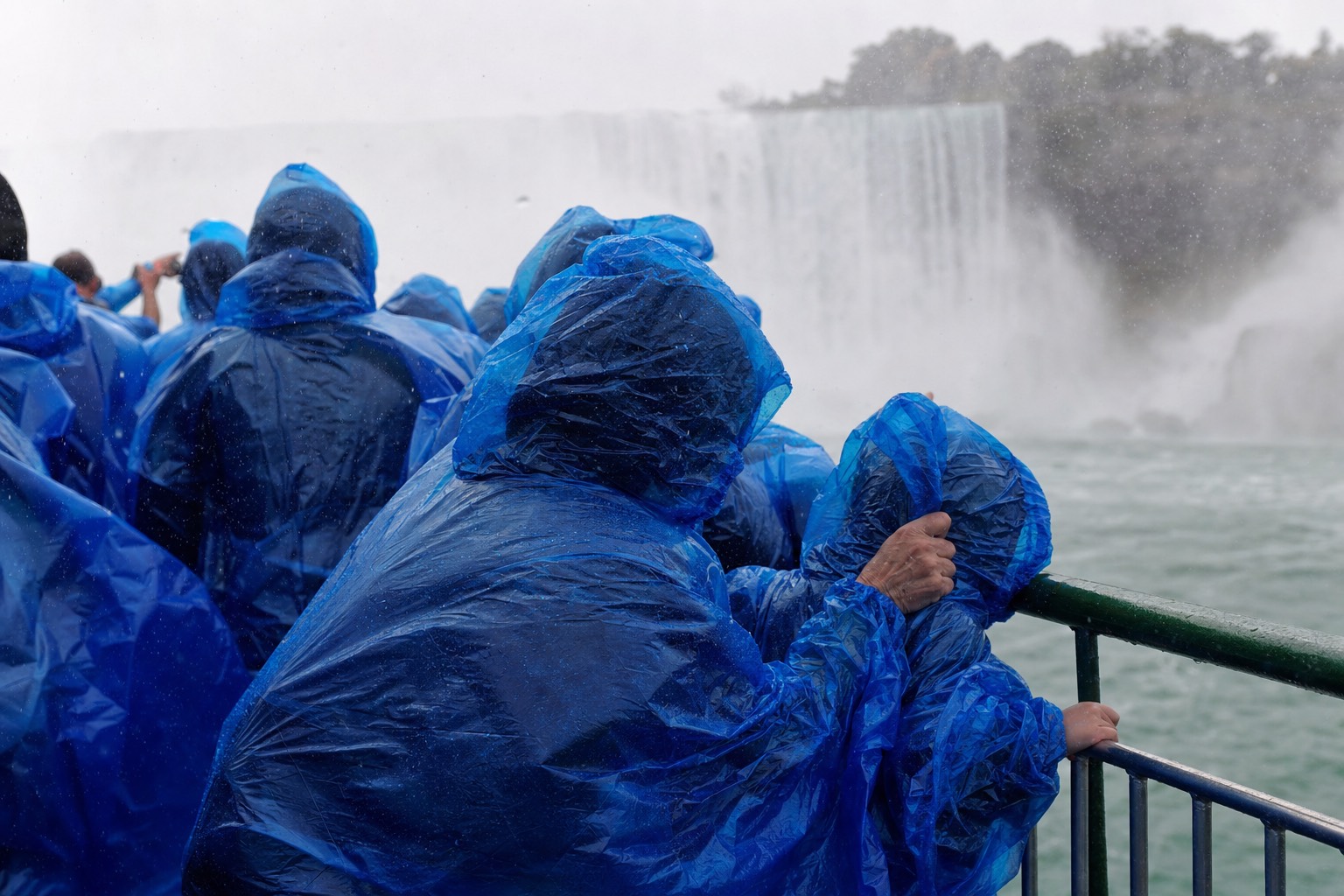 A family in blue ponchos at the boat rail, a child holding the hood closed against the spray