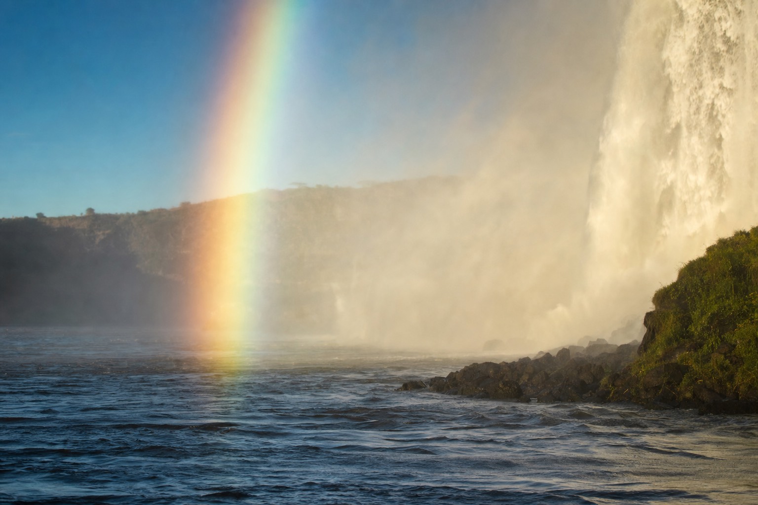 A rainbow standing in the spray column of Horseshoe Falls seen from the water on a clear morning