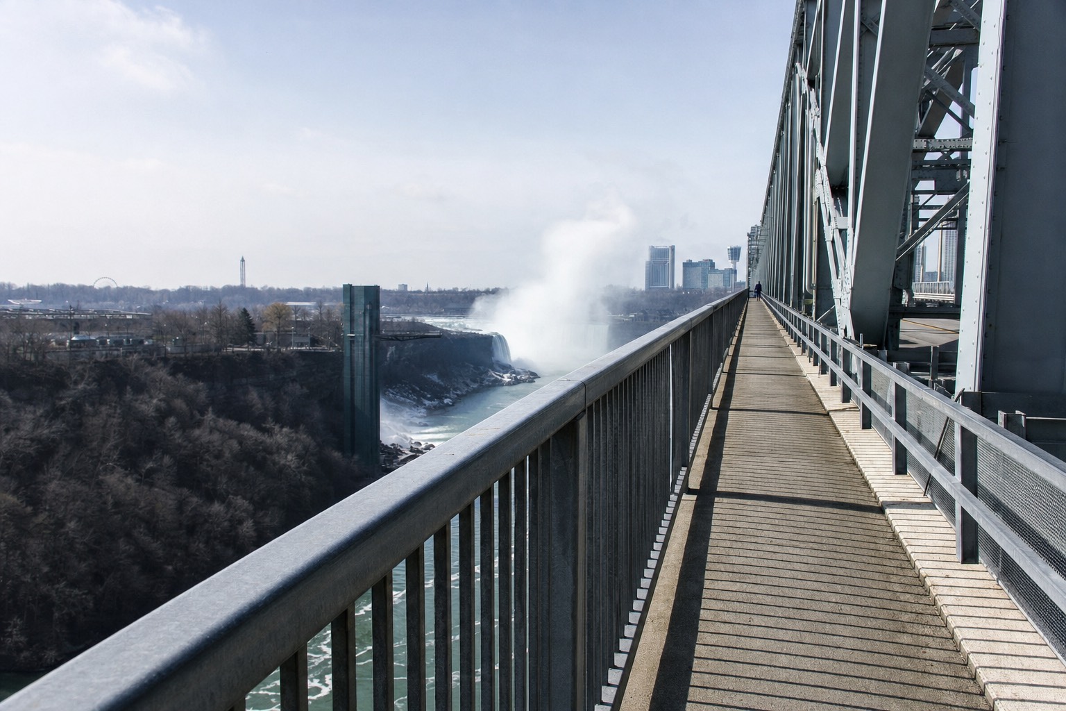 The pedestrian walkway of the Rainbow Bridge with the gorge and falls spray visible beyond the railing