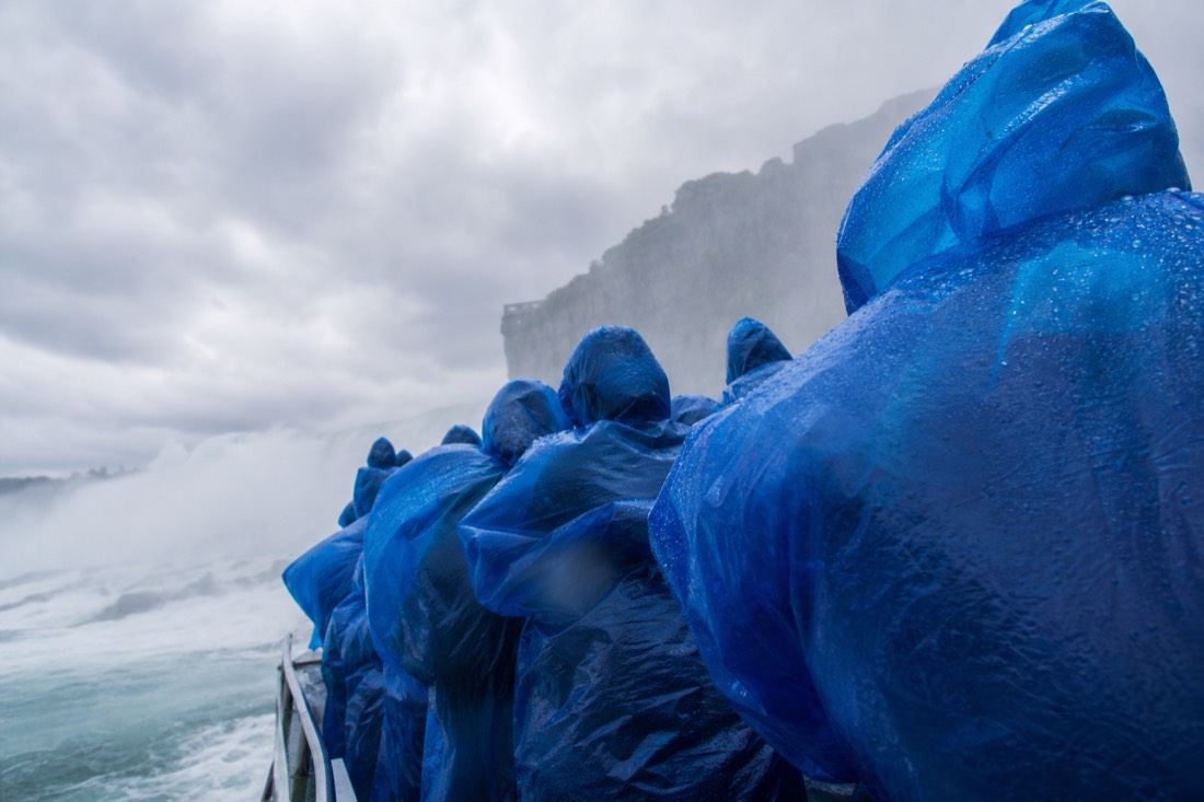 Passengers in blue ponchos on the upper deck of a boat below the falls